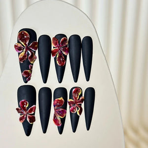 Close-up of matte black long stiletto nails featuring ceramic floral designs.