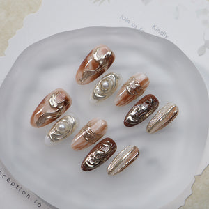 Oval nails with smudged amber tones and metallic details.