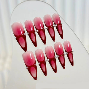 Metal ball-embellished red gradient stiletto nails on display.