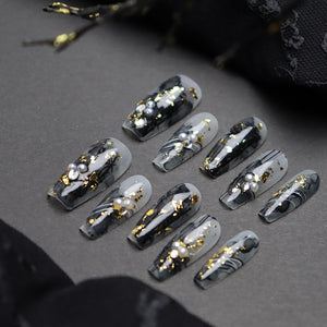 Close-up of luxurious black and gold medium-length coffin nails."