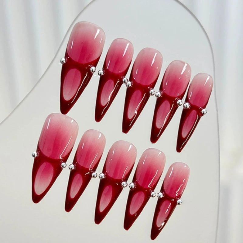 Red ombre stiletto nails with gradient effect and metal ball accents.