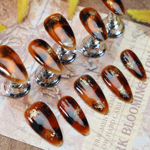 Oval-shaped amber nails with artisanal gold flecks for a chic look.