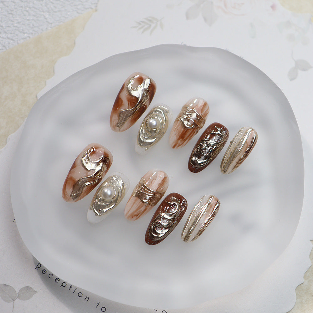 Amber-inspired oval nails with metallic accents and pearls.