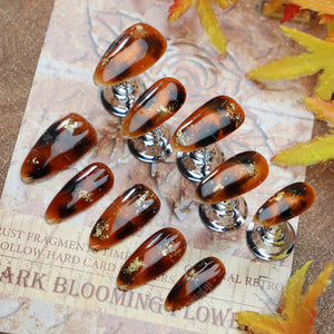 Amber-tone nails with gold details displayed on a rustic background.