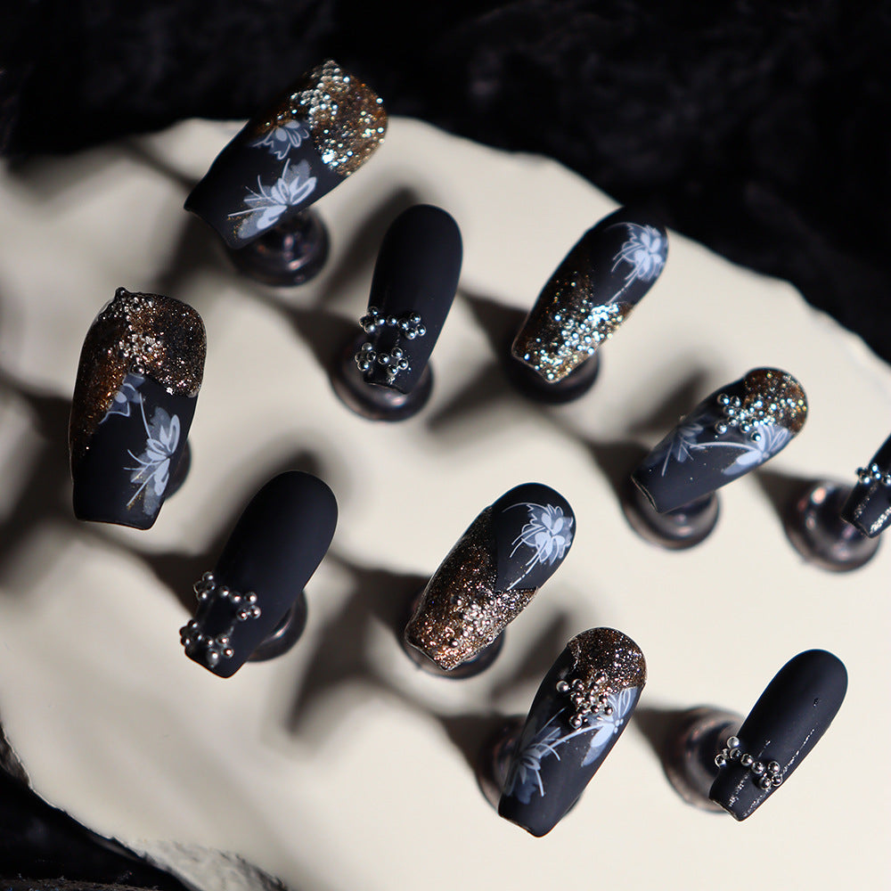 Long matte black nails adorned with floral designs and shimmering glitter.